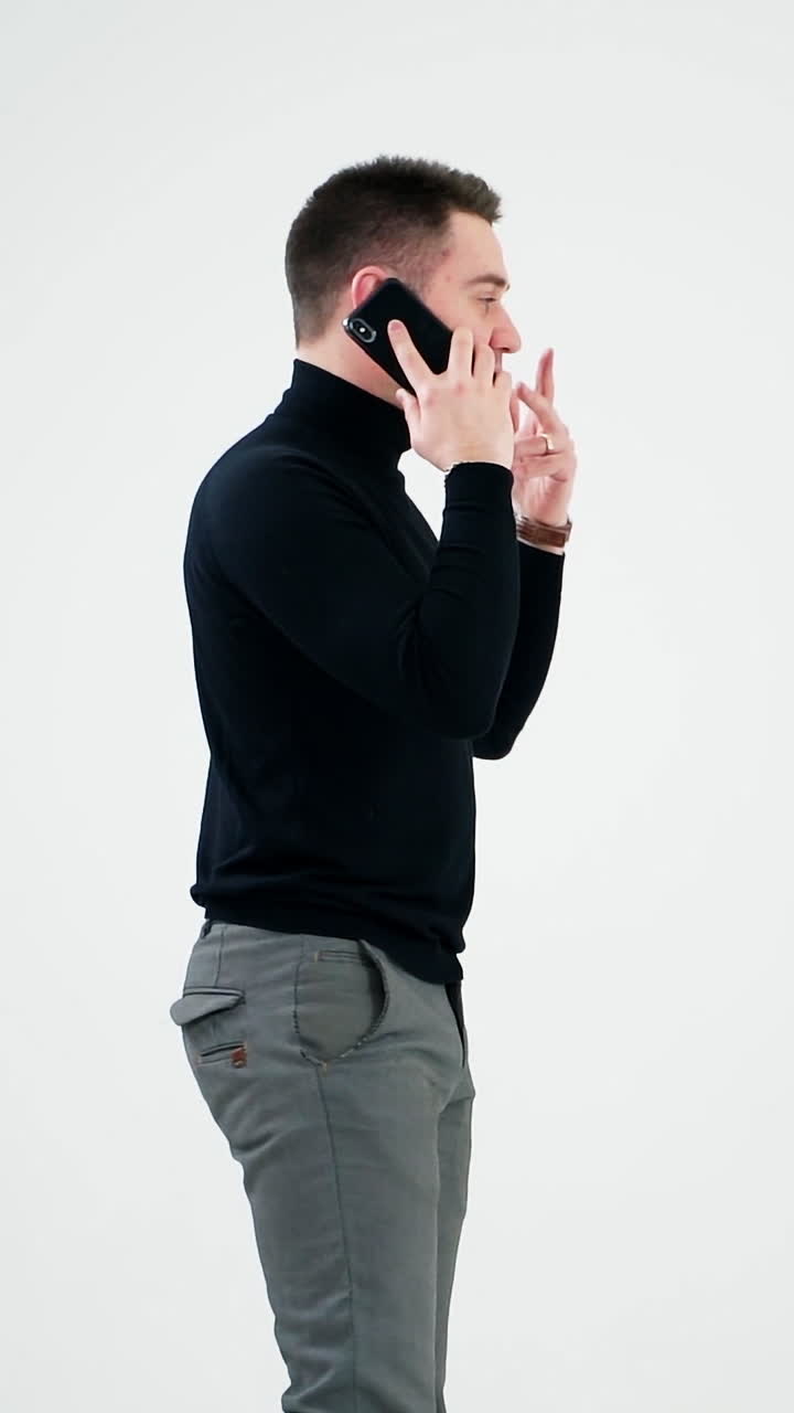 Young businessman talking on the phone. Handsome man in black sweater and grey trousers leading e-business through the cellphone. Man isolated on white. Vertical video