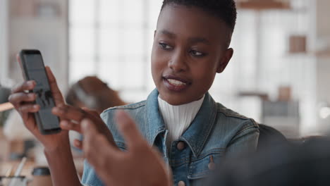 Joven-Mujer-De-Negocios-Afroamericana-Gerente-Usando-Un-Pasante-De-Capacitación-En-Teléfonos-Inteligentes-Apuntando-A-La-Pantalla-Compartiendo-Comentarios-Discutiendo-Ideas-Con-Un-Colega-En-La-Oficina