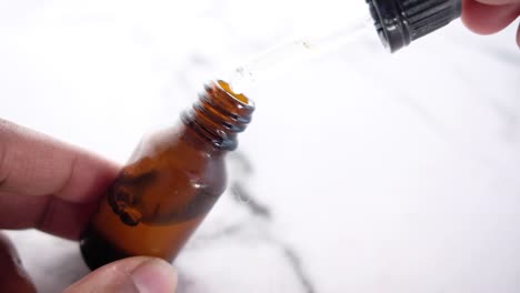 applying oil from a dropper into a brown bottle