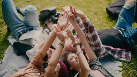 friends touching hands while lying down in park