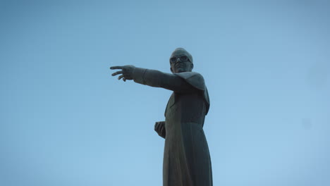 low perspective camera shot of a statue of a priest who is pointing in one direction