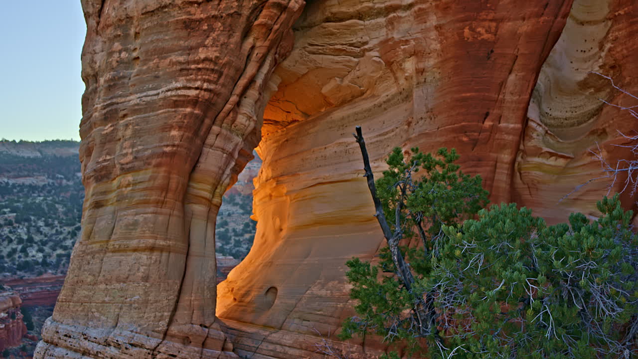Drone glides across a breathtaking red rock landscape, revealing a majestic arch at sunrise.