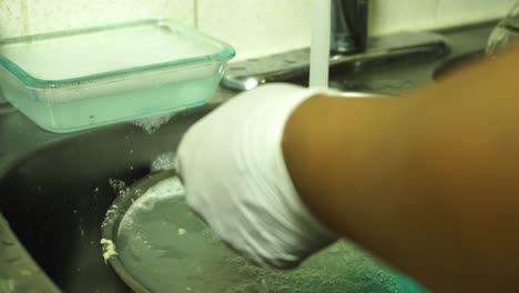 person washing dishes in sink under running water, contributing to the global water crisis