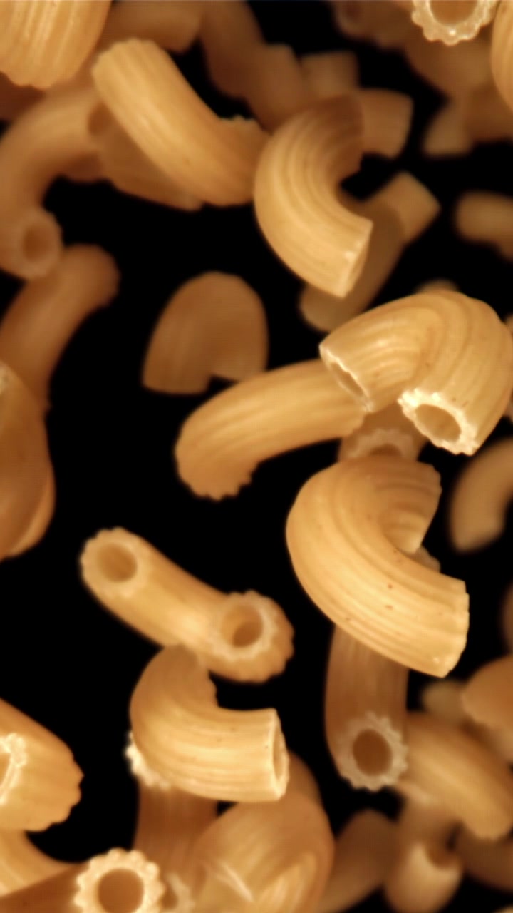 Pasta maccheroni secca che cade al rallentatore su sfondo nero.