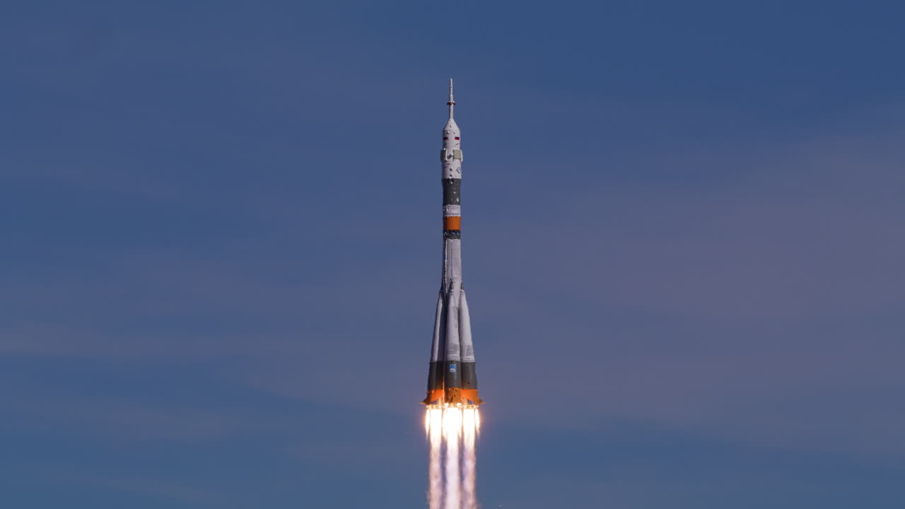 A Soyuz rocket launches from the launchpad, ascending into the sky. Engines ignite with smoke and fire