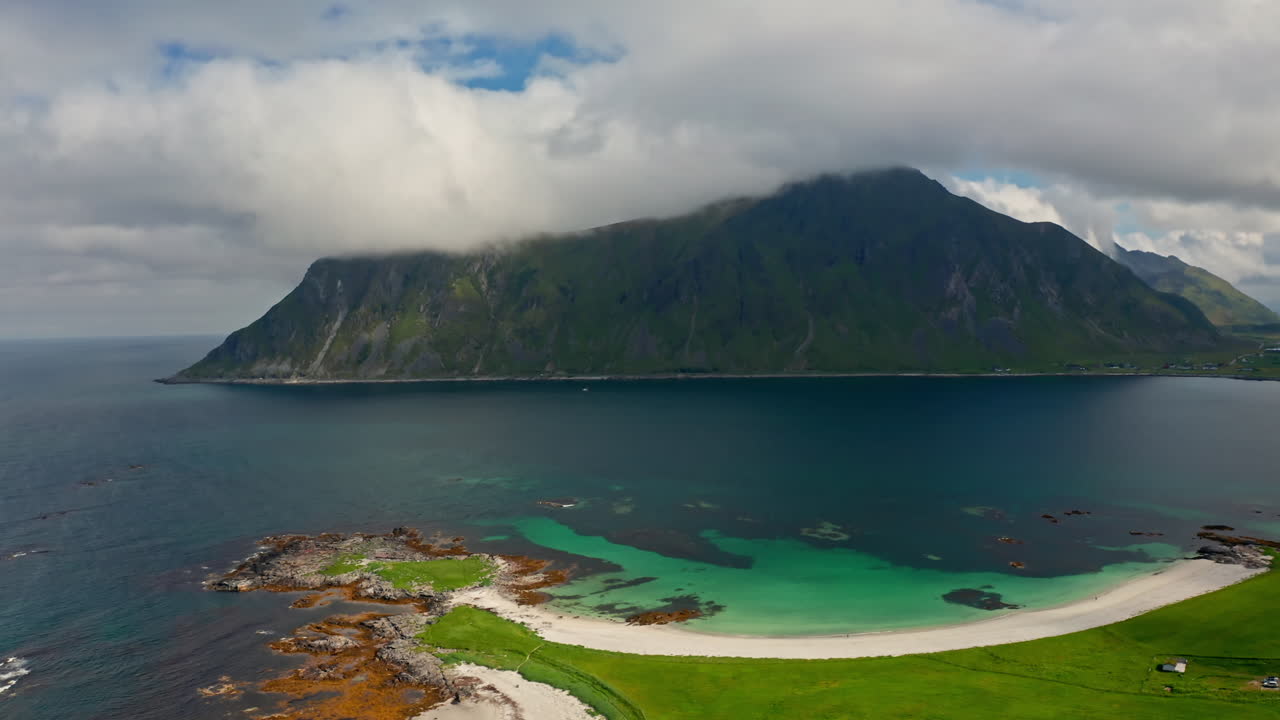 Aerial drone shot over the scenic Nordic Landscape of the Lofoten Islands in Norway. High view of green fields and the long stretching white sanded beach and the turquoise sea.