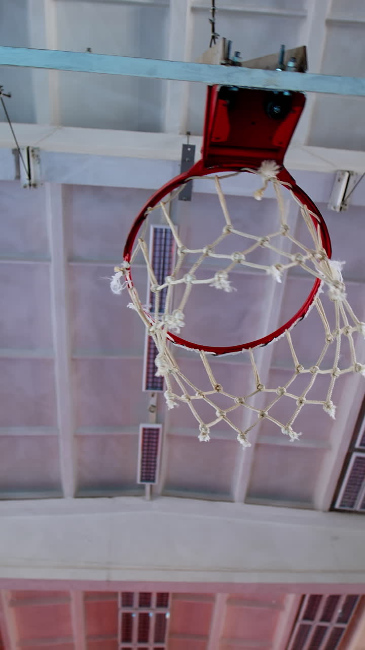 Basketball hoop on empty court. Upward view of basketball hoop indoors. Vertical video
