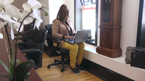 empleador afroamericano con anteojos sentado junto a una ventana grande en la sala de conferencias trabajando en la computadora