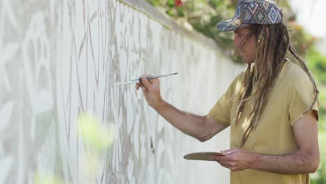 video de un artista masculino caucásico sonriente con rastas pintando un mural en la pared