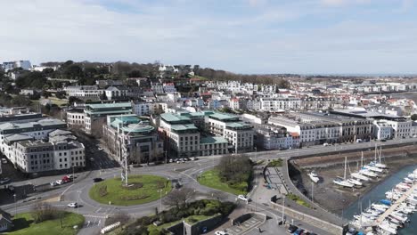 Vuelo-Sobre-North-Beach-Y-Un-Asta-De-Bandera-En-La-Rotonda-De-St-Julian&#39;s-Avenue-Que-Muestra-El-Paseo-Marítimo-Y-Los-Edificios-Comerciales-De-St-Peter-Port-Guernsey-En-Un-Día-Soleado