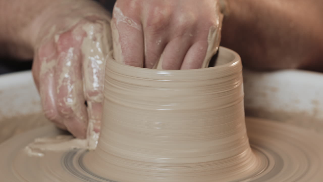Hands shaping a clay pot on a pottery wheel
