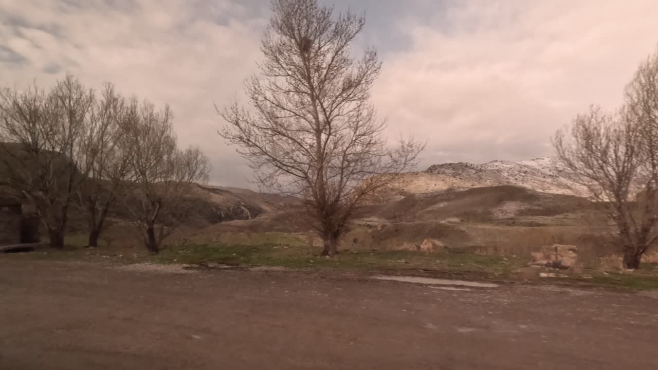 Un viaggio attraverso la Turchia mostra vaste colline e valli sotto cieli nuvolosi. Il terreno roccioso è misto ad arbusti e segni di neve. La natura svela la sua bellezza in questa zona.