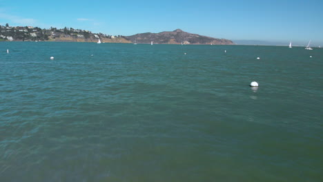 Drone-Volando-A-Baja-Altura-A-Lo-Largo-Del-Agua-Del-Puerto-De-Sasalito-Al-Otro-Lado-De-La-Bahía-Desde-San-Francisco