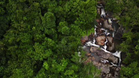 drone aerial camera flying along a mountain waterfall and dense greenery in thailand's evergreen than sadet waterfall region