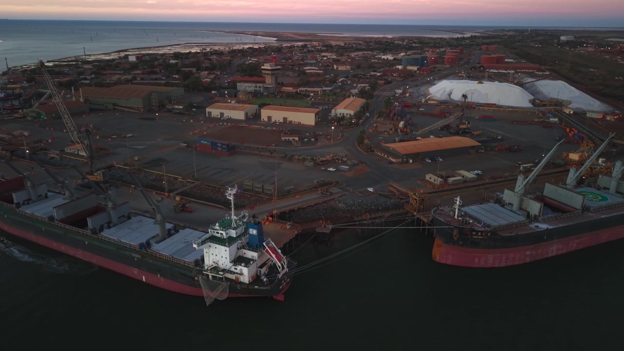 Pengiriman Sumber Daya Port Hedland. Ekskavator di gundukan garam dari udara dengan kapal-kapal di latar depan.