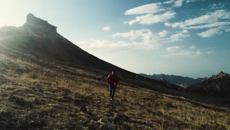 Young-athletic-man-runs-towards-aerial-drone-camera,-behind-scenic-mountain-landscape-at-golden-hour,-dolly-out