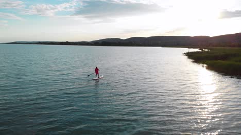 aerial of a woman on a stand up paddle board during sunset