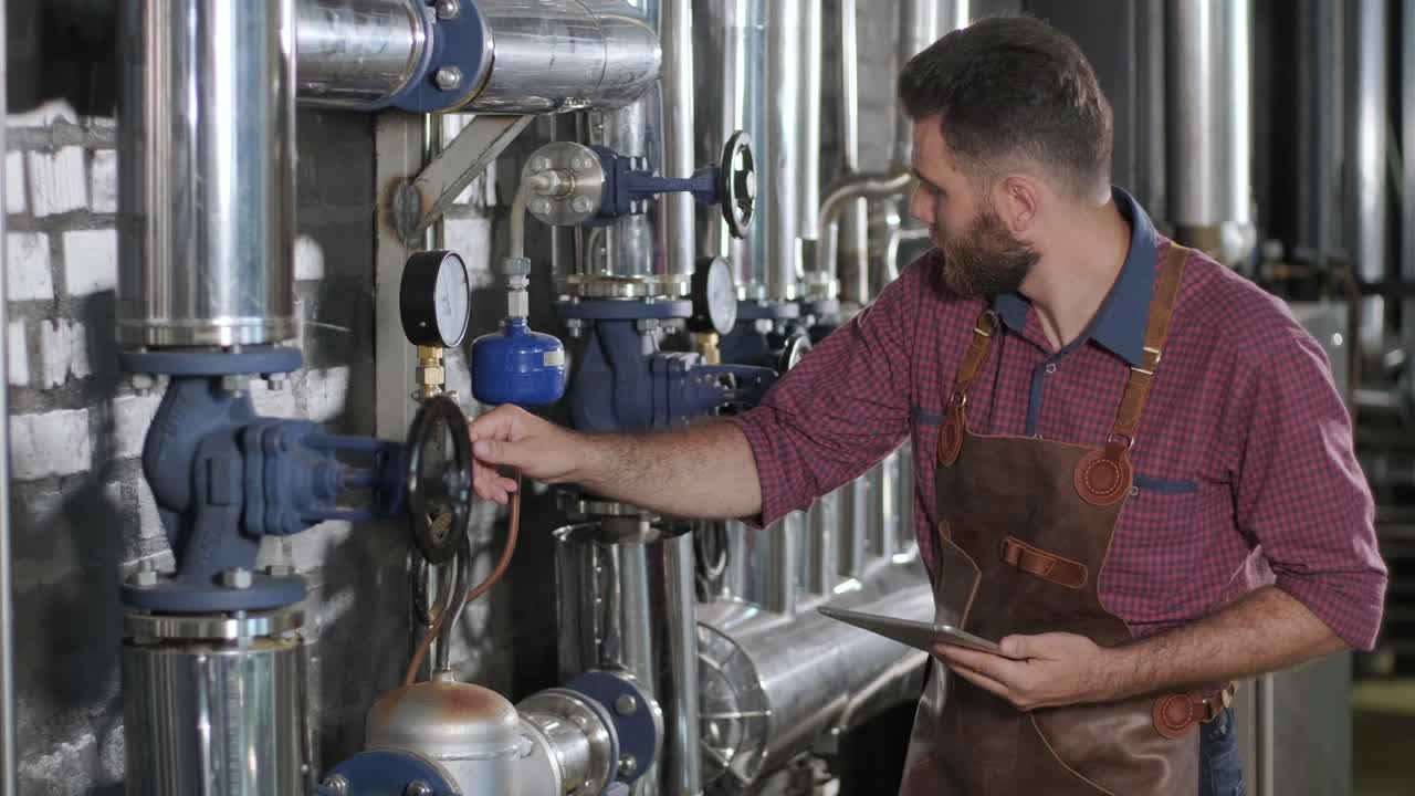 un joven cervecero con un delantal de cuero supervisa el proceso de fermentación de la cerveza en una fábrica de cerveza moderna
