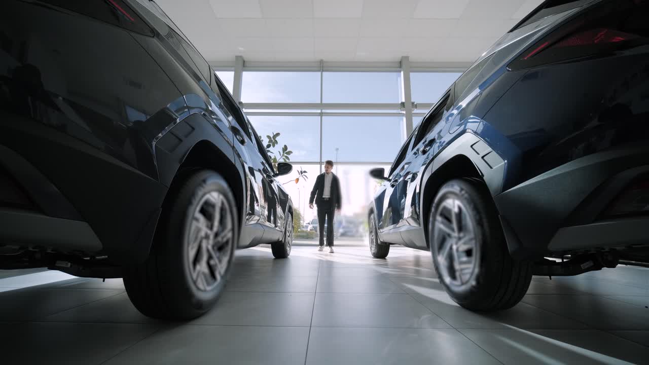 A man standing between two cars in a car dealership