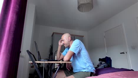 side view of a man focused on work at a desk within a bedroom setting.