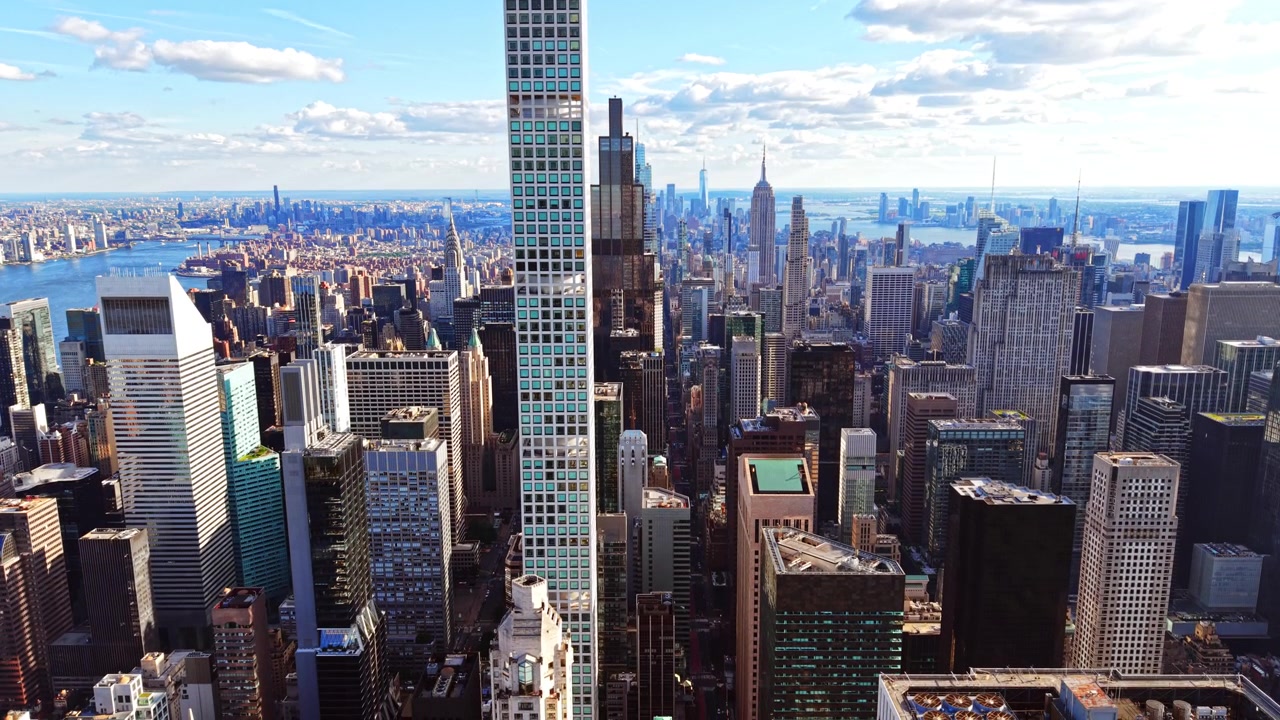 Vista aérea de uma torre residencial esguia, Nova Iorque. Fachada de vidro turquesa eleva-se acima da orla do East River e do horizonte de Midtown à luz do dia.