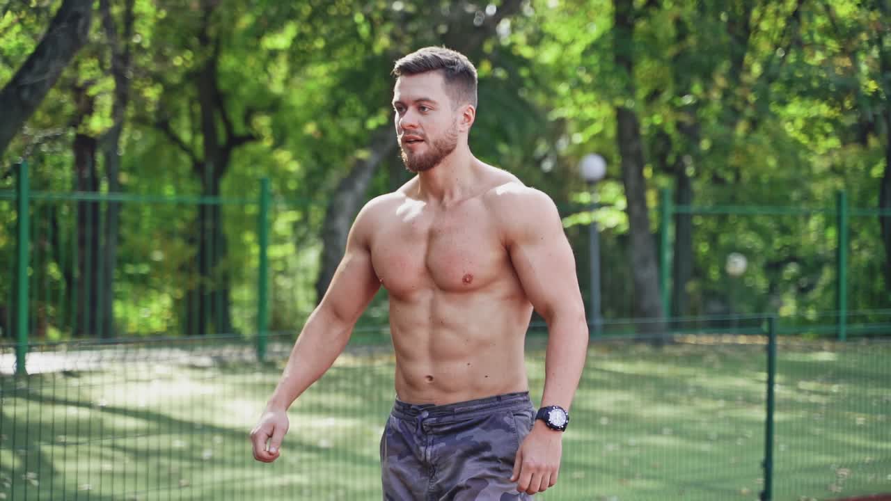 Muscular runner on the outdoor stadium. Portrait of a strong athlete without shirt prepares for running on a track. Slow motion.