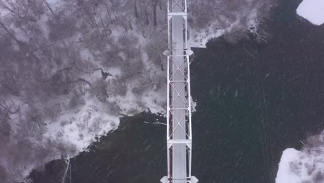 top down aerial view of a bridge crossing a river with snow actively falling