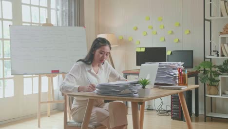 asian woman looking at laptop and taking note while working with documents at the office