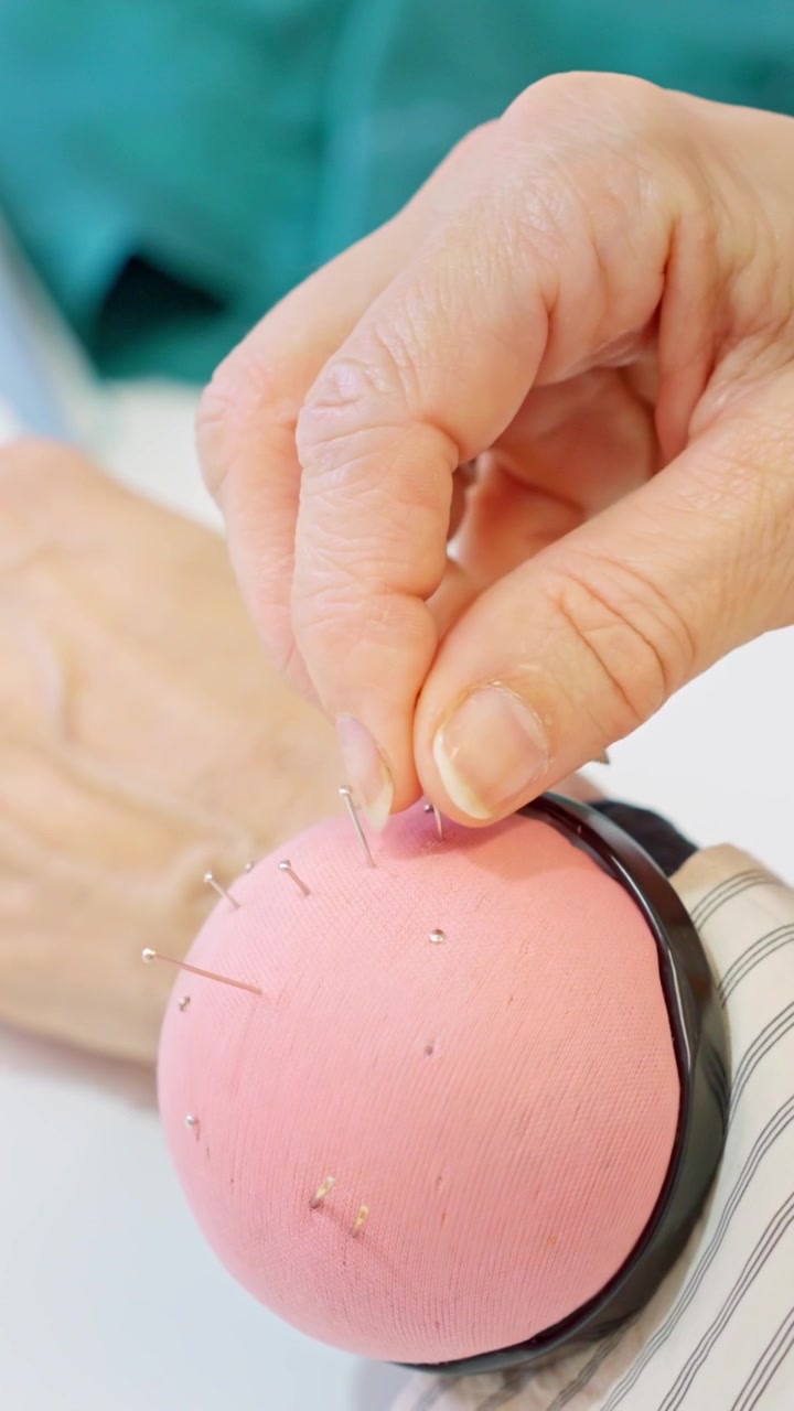 Seamstress taking a pin from a pincushion