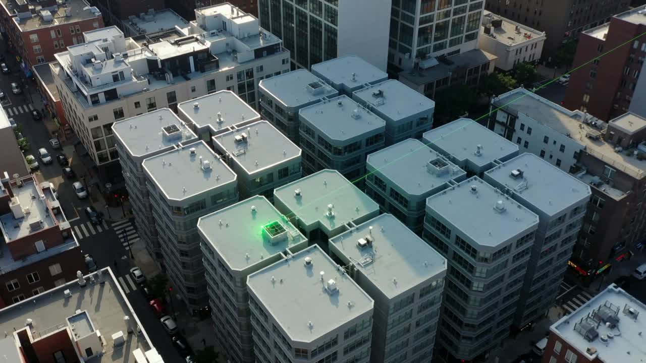 Telecamera aerea che panoramica rivelando tetti urbani di media altezza con bocchette di ventilazione, evidenziando un'unità verde pulsante.