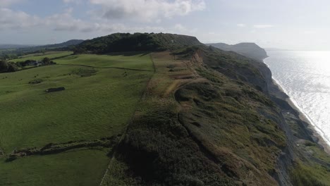 Los-Acantilados-De-Golden-Cap-Y-Charmouth-Beach-Se-Revelan-Con-Una-Pista-Aérea-Desde-El-Interior-Hacia-El-Mar-Mirando-Hacia-El-Este