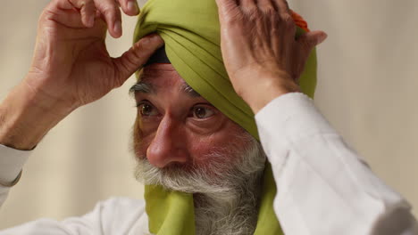 prise de vue rapprochée d'un homme sikh âgé à la barbe utilisant l'aiguille salai lorsqu'il porte un turban contre un fond plat 1