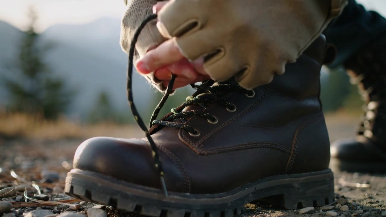 Tangan pendaki tanpa jari mengencangkan, menarik, dan mengikat tali sepatu bot kulit di jalur, bersiap untuk mendaki