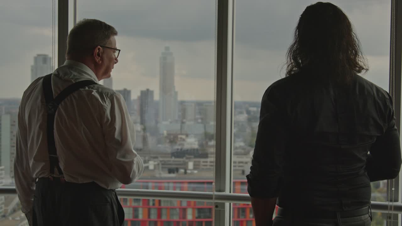 Medium view of an older businessman points towards the city skyline of Rotterdam, the Netherlands while talking to an employee