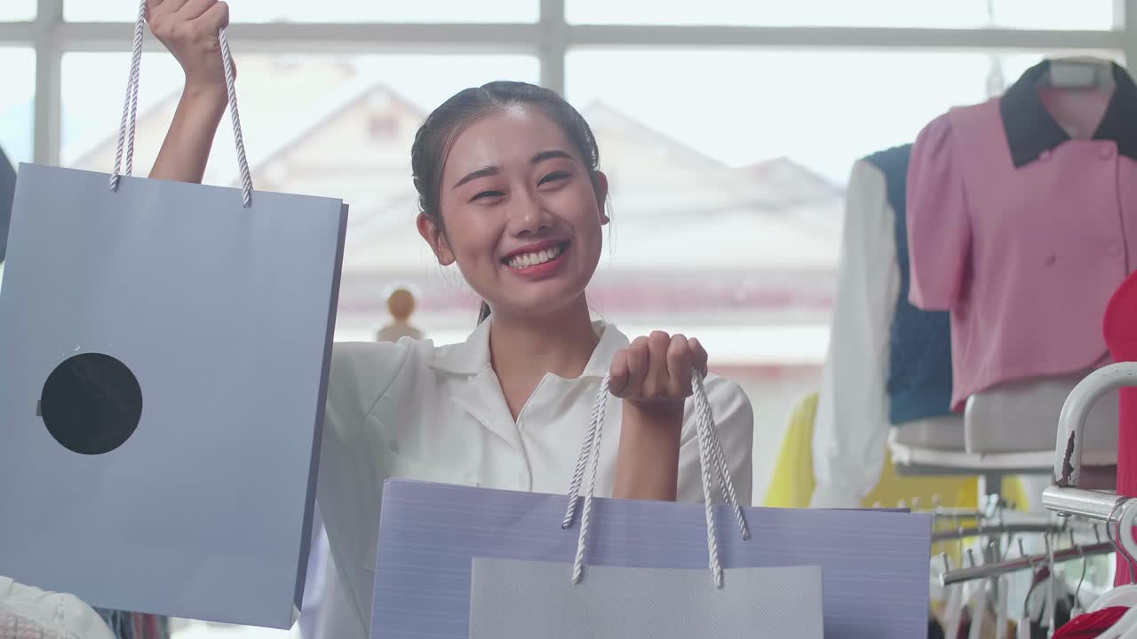 부티크에서 쇼핑하는 동안 카메라에 미소 짓는 쇼핑 가방을 가진 젊은 아시아 여성