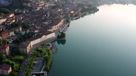 Drone-view-of-Lake-Iseo-at-sunrise,-on-the-left-the-city-of-Lovere-which-runs-along-the-lake,Bergamo-Italy