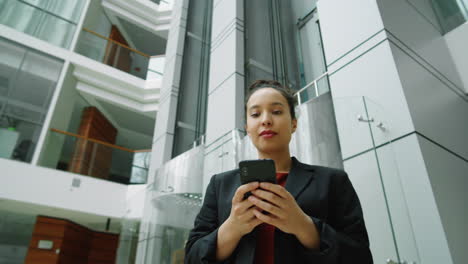 mujer de negocios caminando en el centro de oficinas y usando un teléfono inteligente