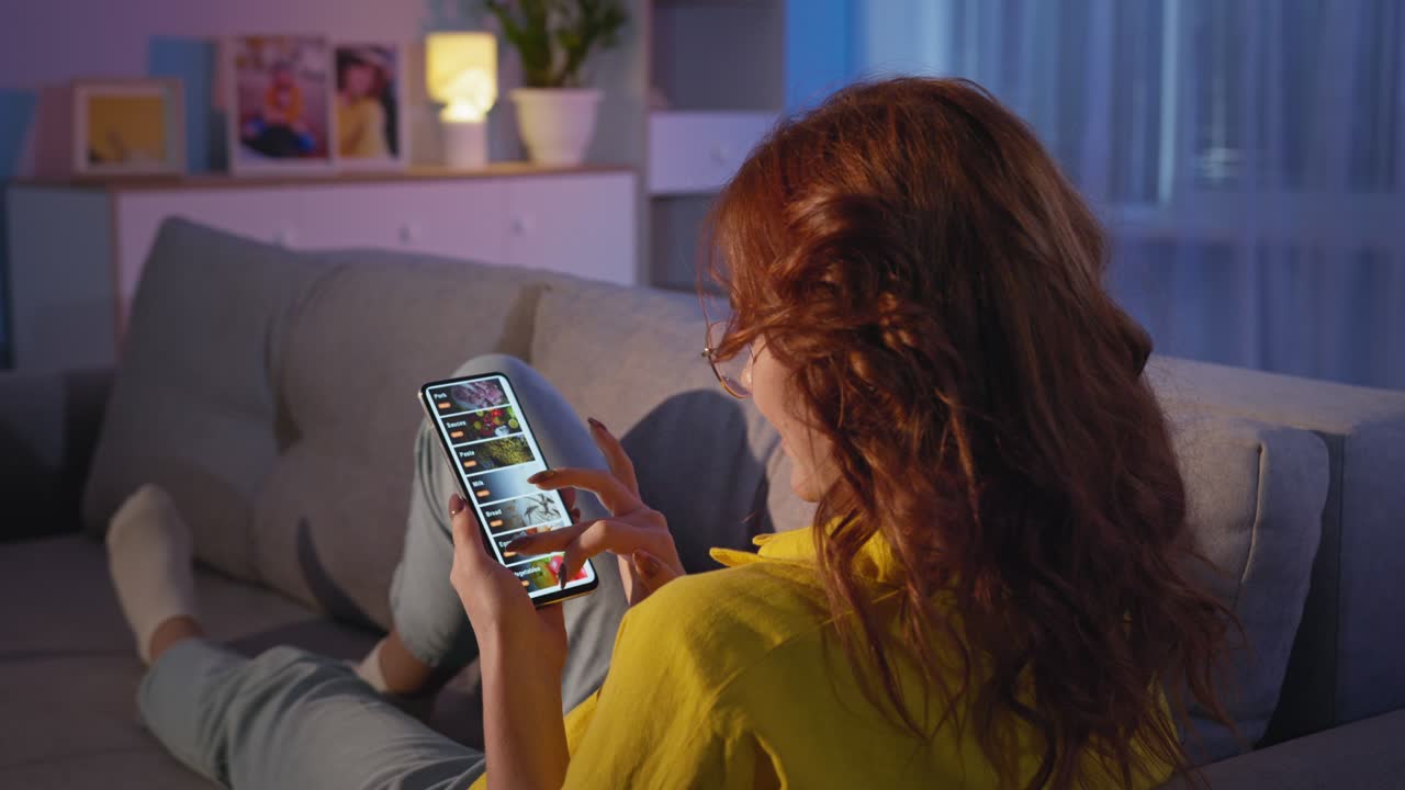 stay at home, young woman orders groceries from an online store with home delivery while relaxing on living room couch in evening