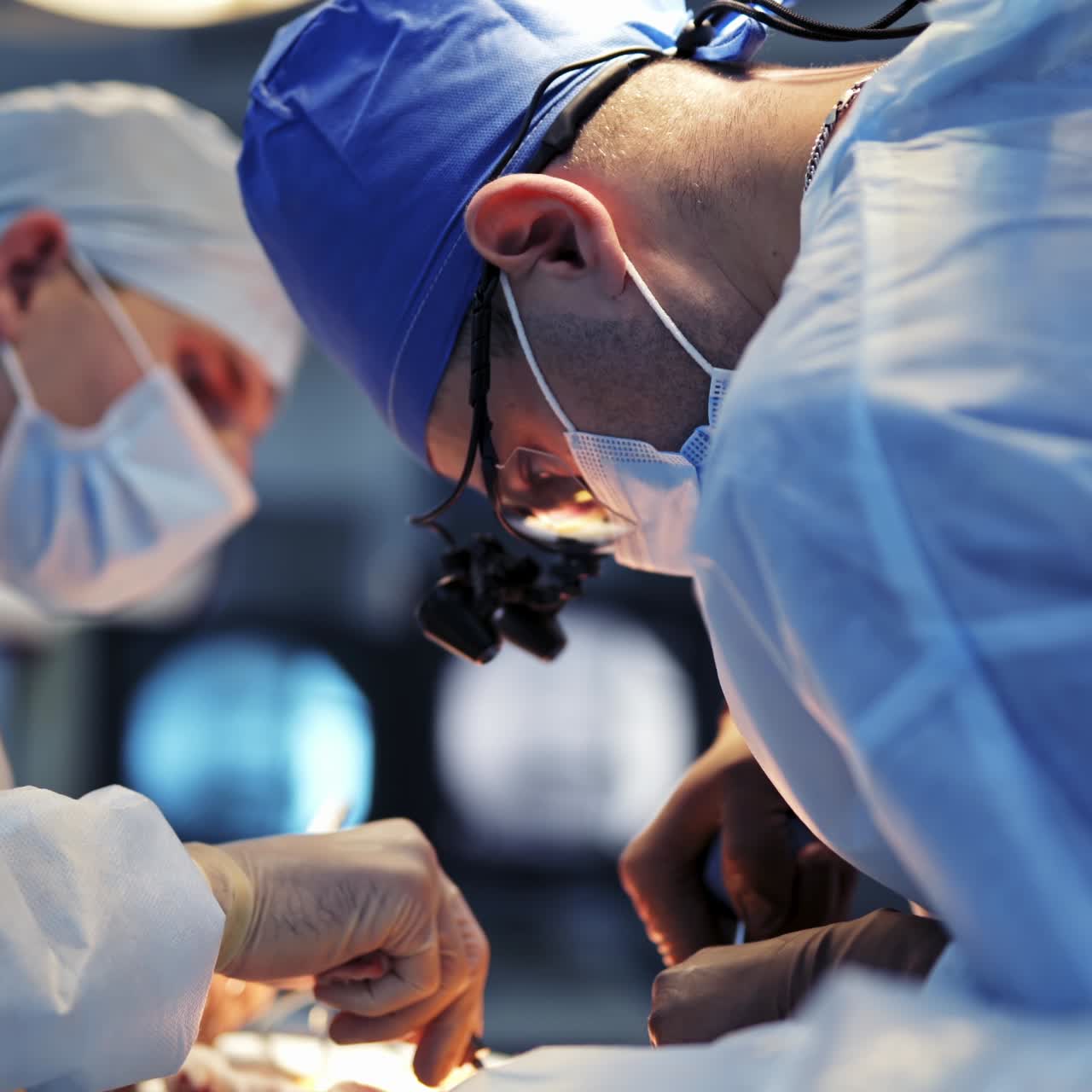 Neurokirurger i ansigtsmasker og operationsbriller opererer patient med specielle instrumenter. Medicinsk personale i operationsdragt filmer fra selektiv vinkel.