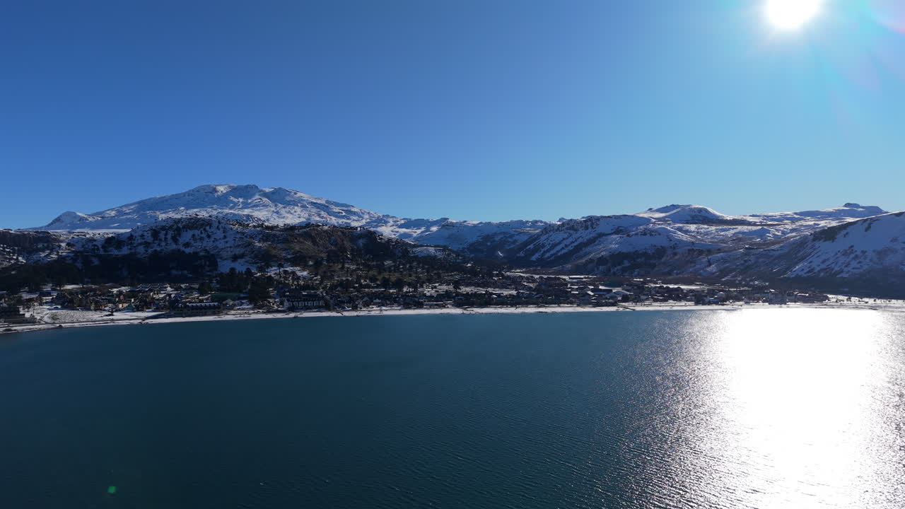 Baia calma e bellissima del Lago Caviahue che riflette i raggi del sole davanti a montagne innevate sullo sfondo a Caviahue, Neuquén, Argentina
