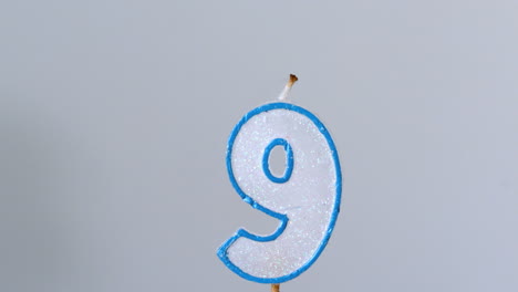 Nine-birthday-candle-flickering-and-extinguishing-on-blue-background