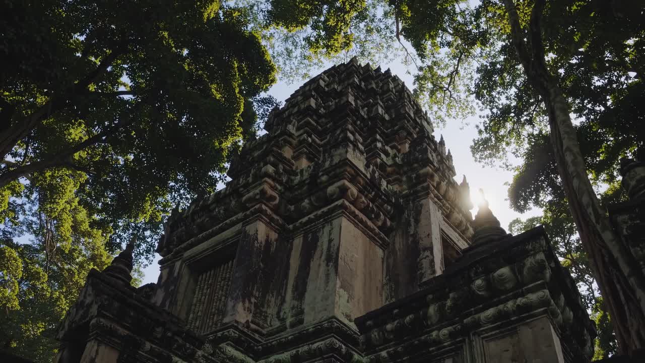 Low-angle video shot of an ancient stone temple surrounded by lush trees, capturing the majestic