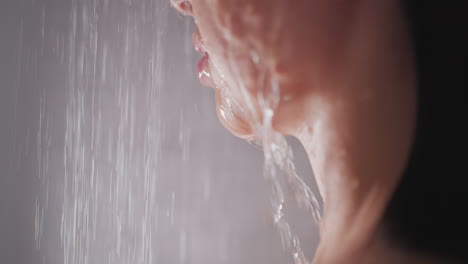 water pours on woman face in bathroom closeup. sensual lady with plump lips takes warm shower in washroom. beauty and glamour lifestyle concept