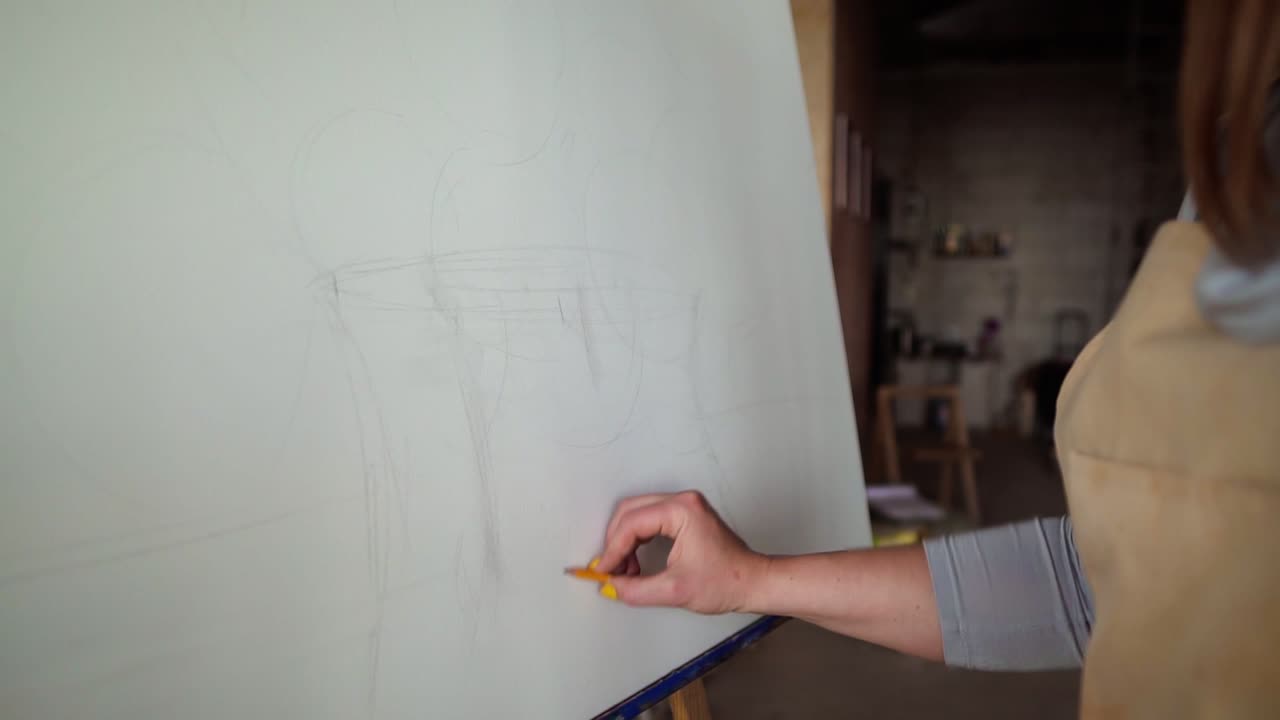 mujer joven diseñadora irreconocible en delantal beige dibujando un boceto en lienzo usando lápiz gris medio disparado
