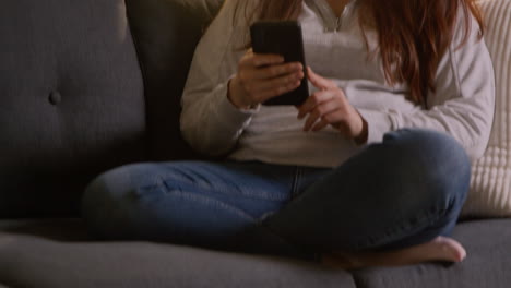 Woman-Wearing-Wireless-Headphones-Sitting-On-Sofa-At-Home-Streaming-Music-From-Mobile-Phone-3