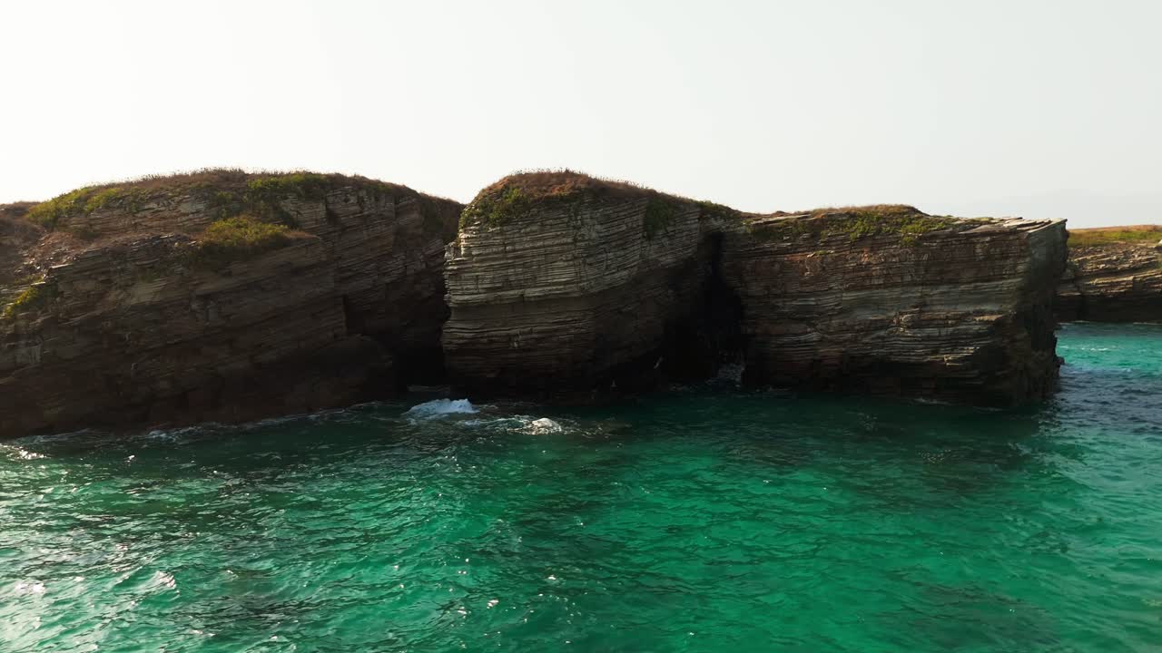 Rocky coastal cliffs with natural stone arches rising above clear turquoise waters