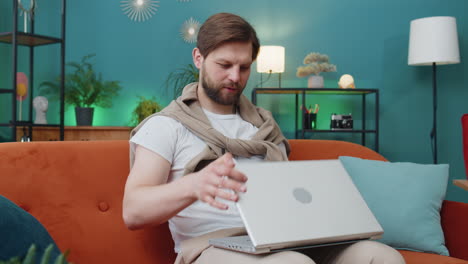 young man freelancer sitting on couch closing laptop pc after finishing work in living room at home