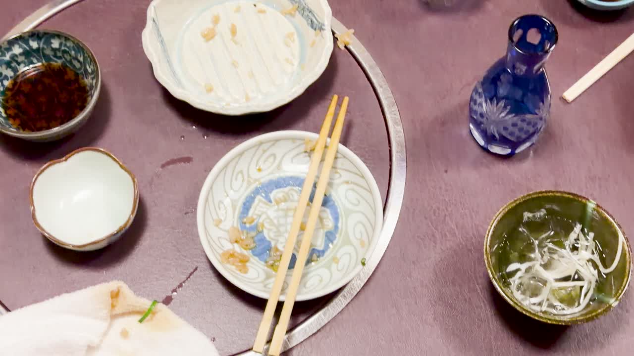 Overhead camera pans across a restaurant table with finished plates, chopsticks, and soy sauce