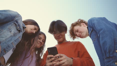 a group of teenagers with two girls and two boys watching something hilarious on the screen of a mobile phone