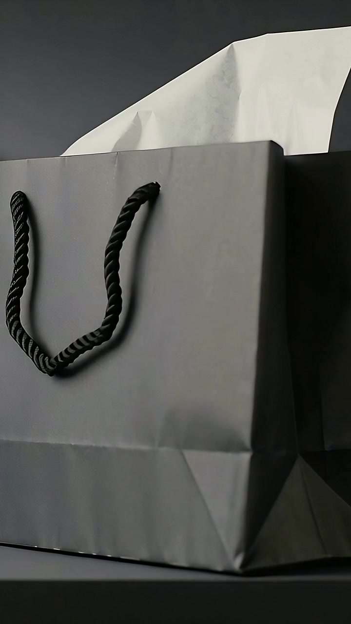 Video verticale: panoramica della fotocamera che mostra una borsa nera opaca con manici in corda e carta velina bianca per una pubblicità